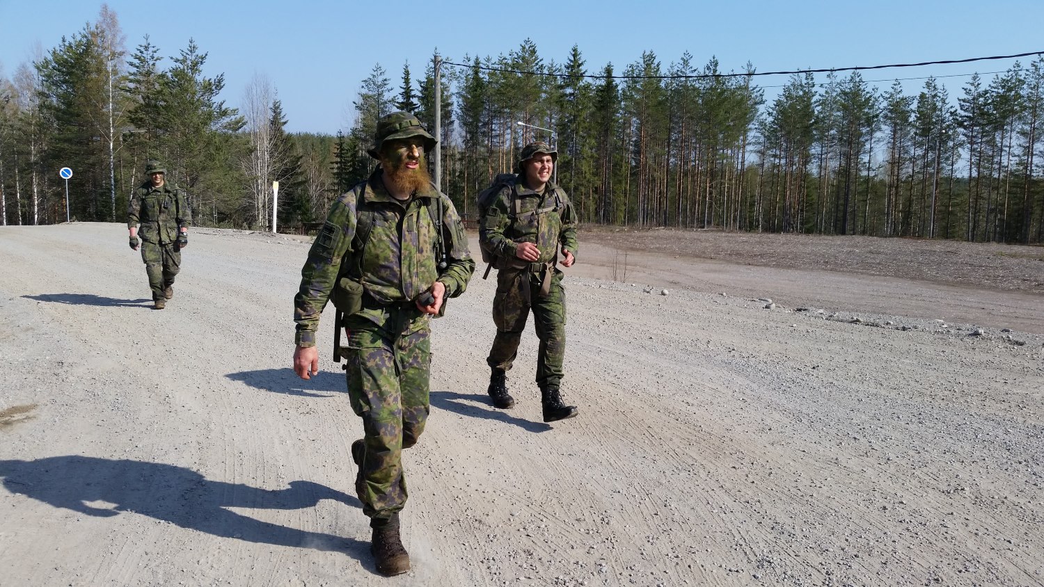 Three people walking on a dirt road in camouflage clothing.