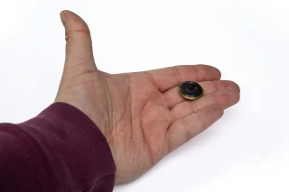 Großer Messingknopf. Die Rückseite ist entweder aus schwarzem oder metallfarbenem Stahl.