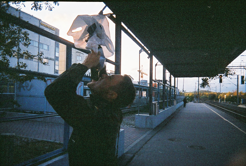 A man on a train stop holding a plastic bag above his head and liquid coming out into his mouth.