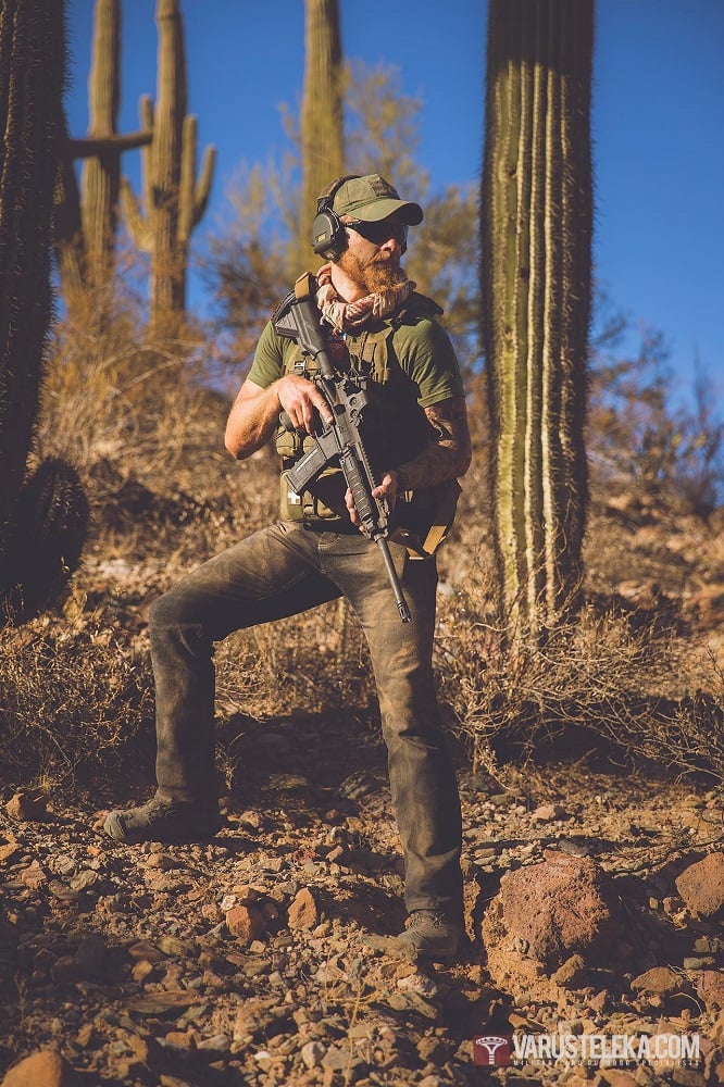 A figter standin in a desert surrounded by bushes and large cactae, holding an assault rifle.
