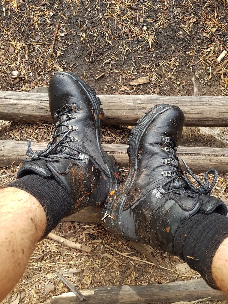 Feet with proper black sturdy hiking boots that seem to have hit some muddy trails.