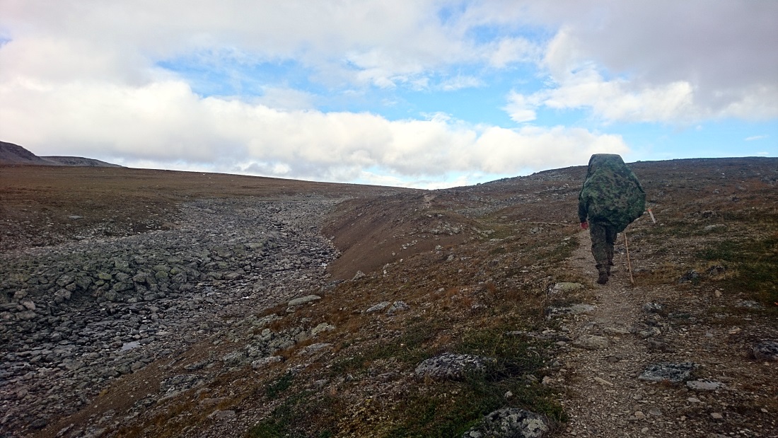 A hiker with a large backpack walking along a stony trail in a rugged environment.