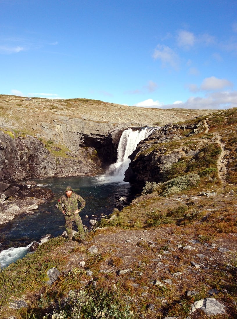 The bearded hiker standing on a cliff with the waterfall as a backdrop.