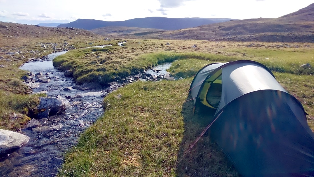 A tent on a creek surrounded by green grass.