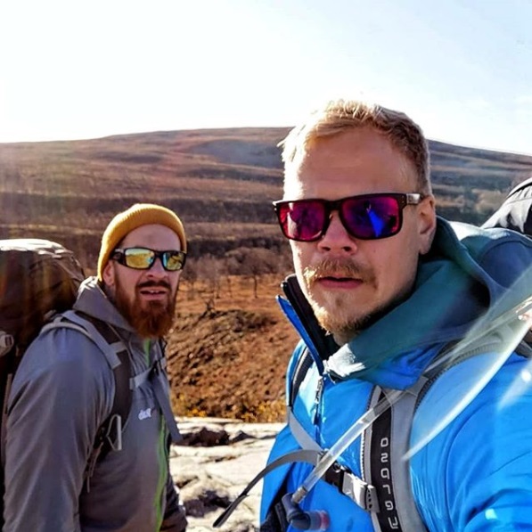 Two men in sunglasses looking at the camera in a mountain landscape.