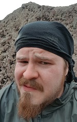 A face of a frowning man in front of a grey hill.