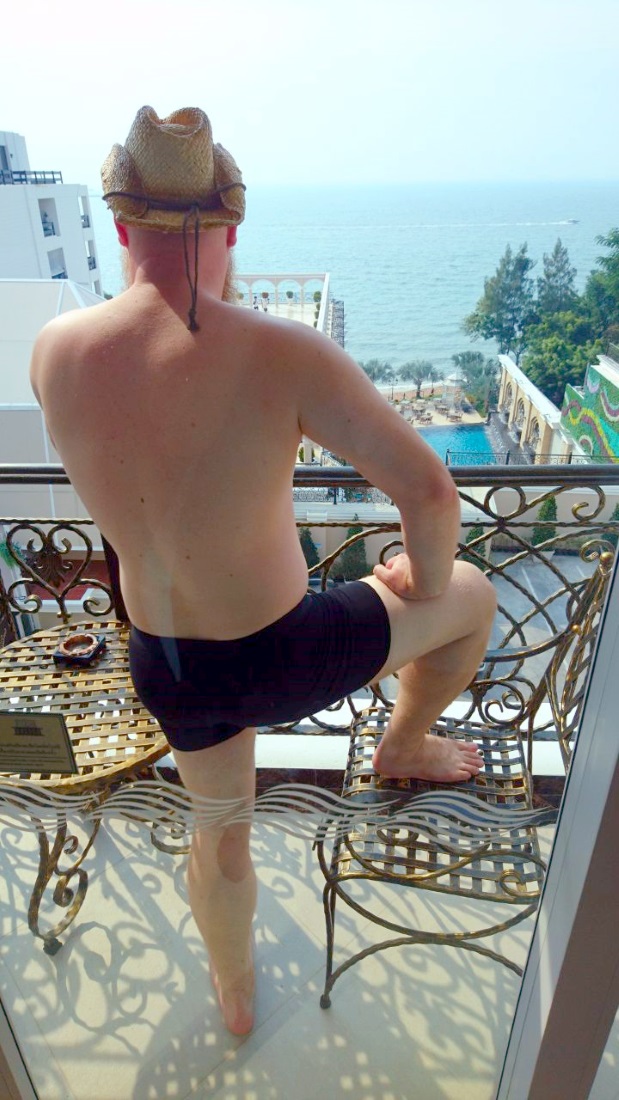 A man in his undies standing on a balcony gazing at the sea.