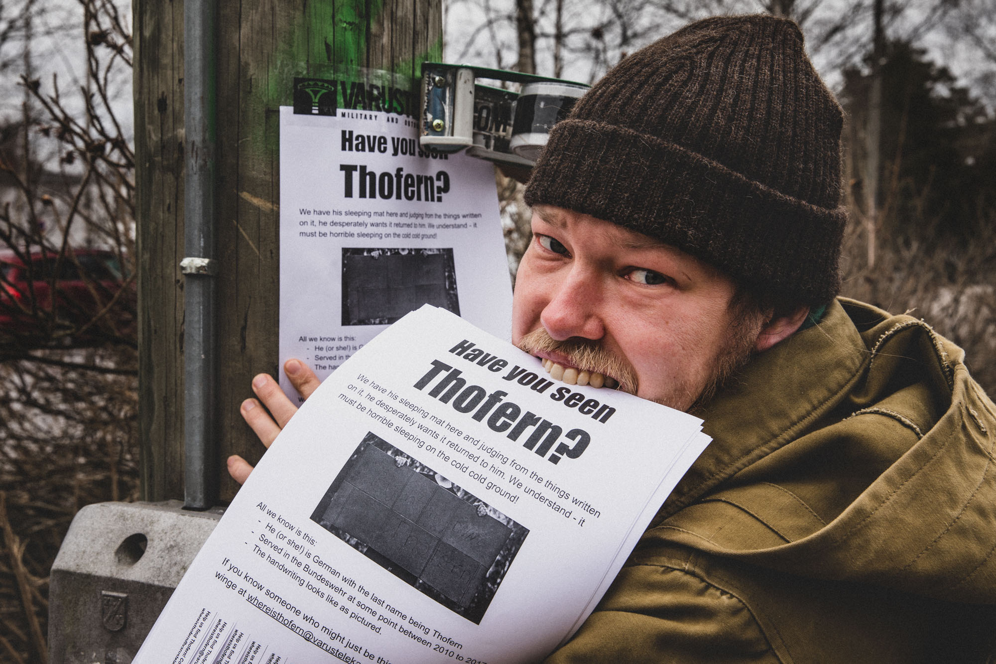 A man outdoors taping Have you seen Thofern? ads to a pole.