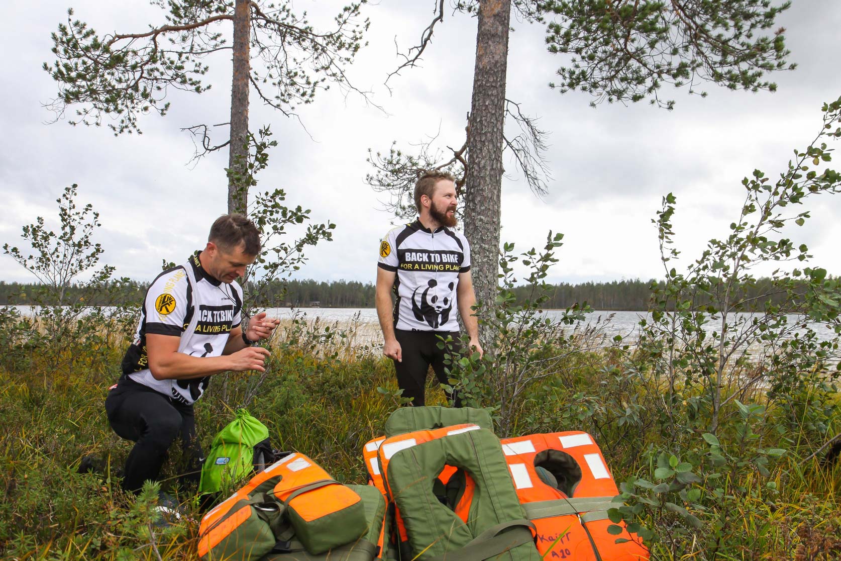 Kaksi miestä vesistön rannalla edessään kassa kelluntaliivejä.