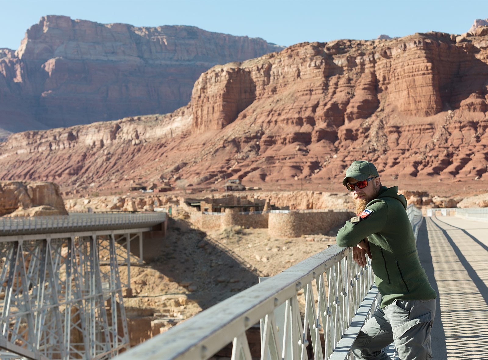 A man leaning on to a bridge railing, surrounded by brown cliffs.