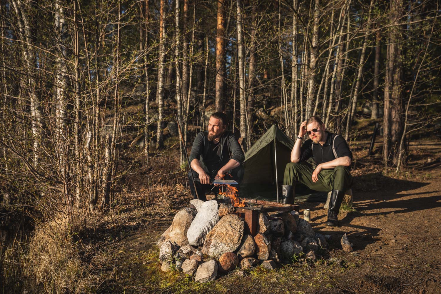 Two men around a campfire in the sunshine.