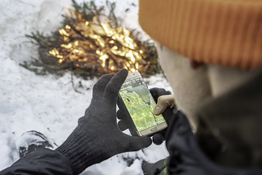 Metsästäjä katsoo karttaa puhelimelta tulilla.