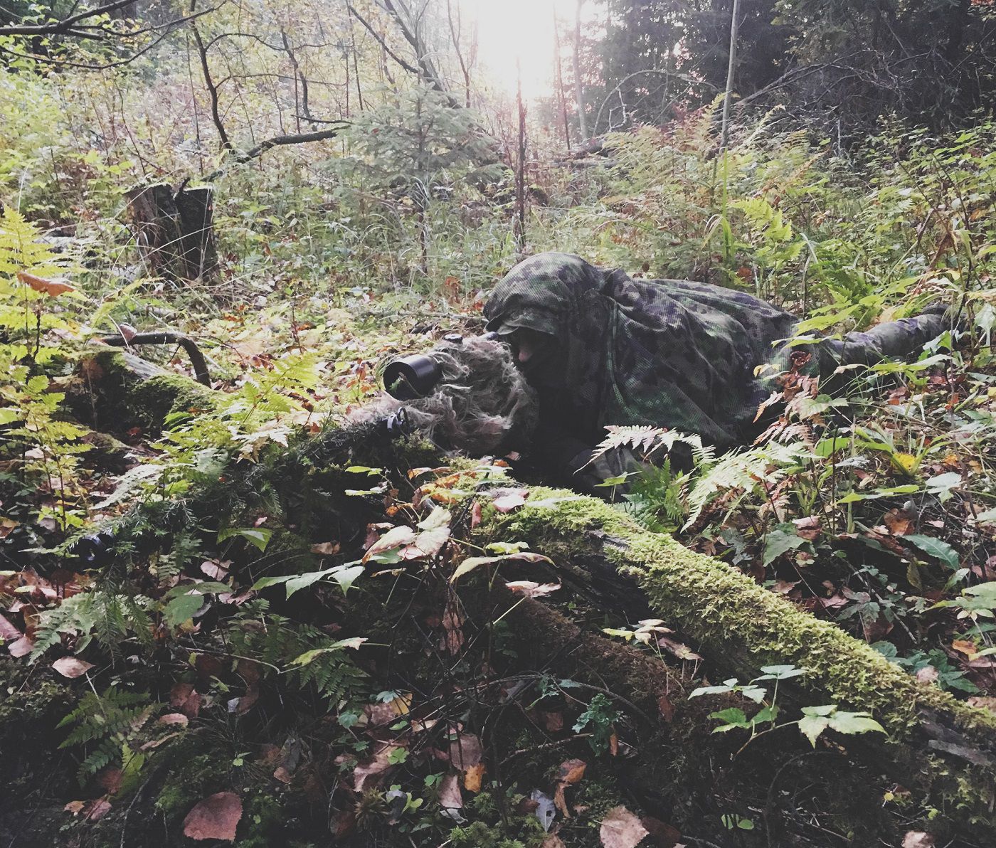 A sniper lying down in the woods with camouflage gear can hardly be spotted from the surroundings.