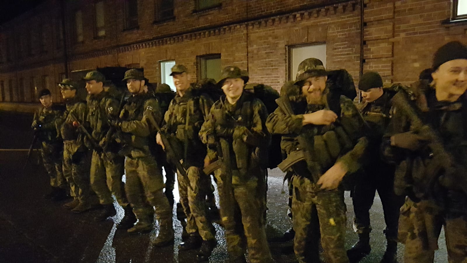 Smiling soldiers in dim light a row in front of the red brick building.