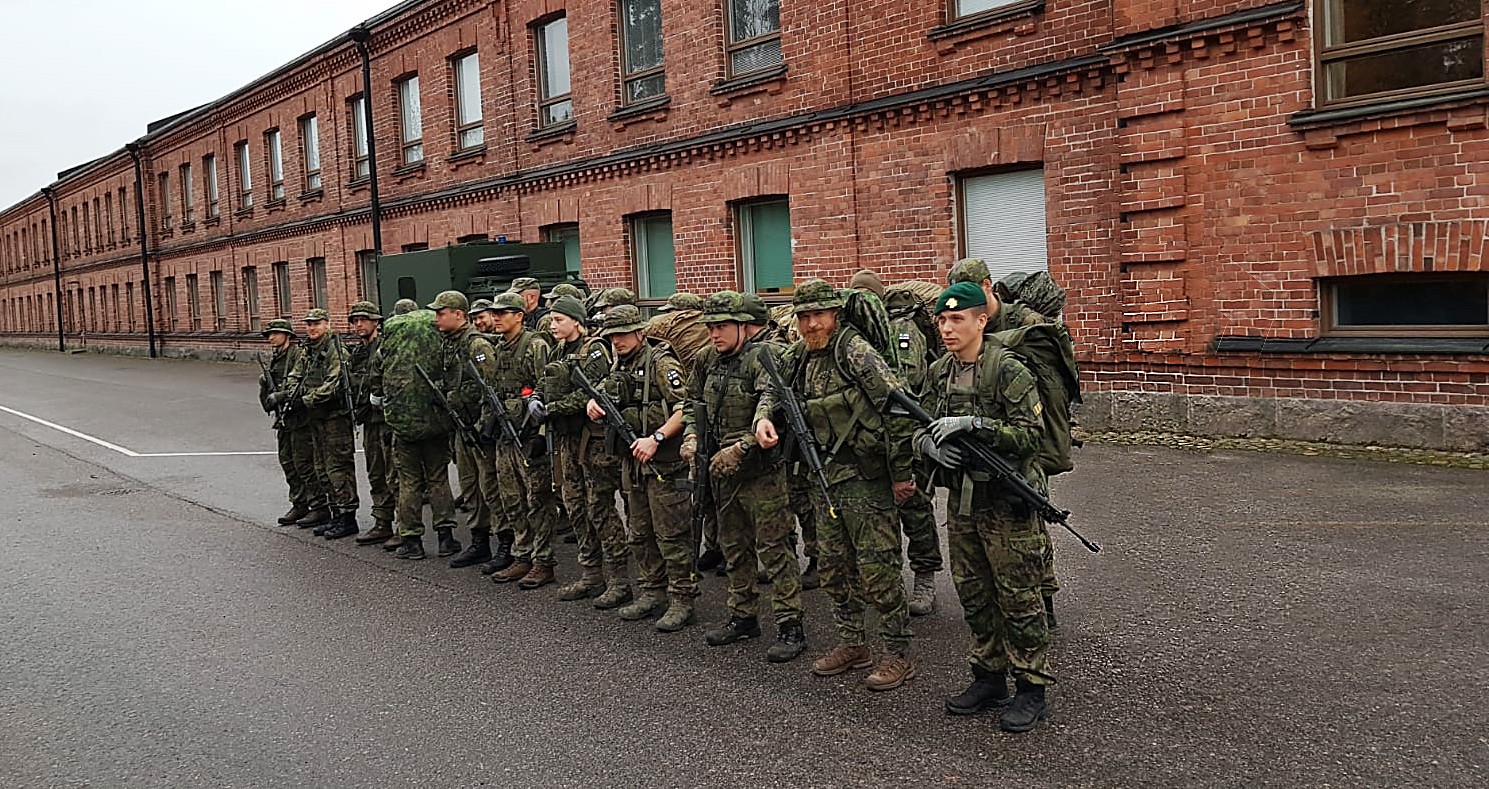 A few dozen soldiers on a row in front of a red brick building.