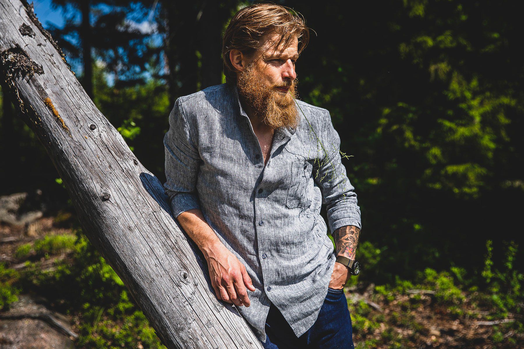 A relaxed bearded and tattooed man wearing a linen shirt and other summer apparel.