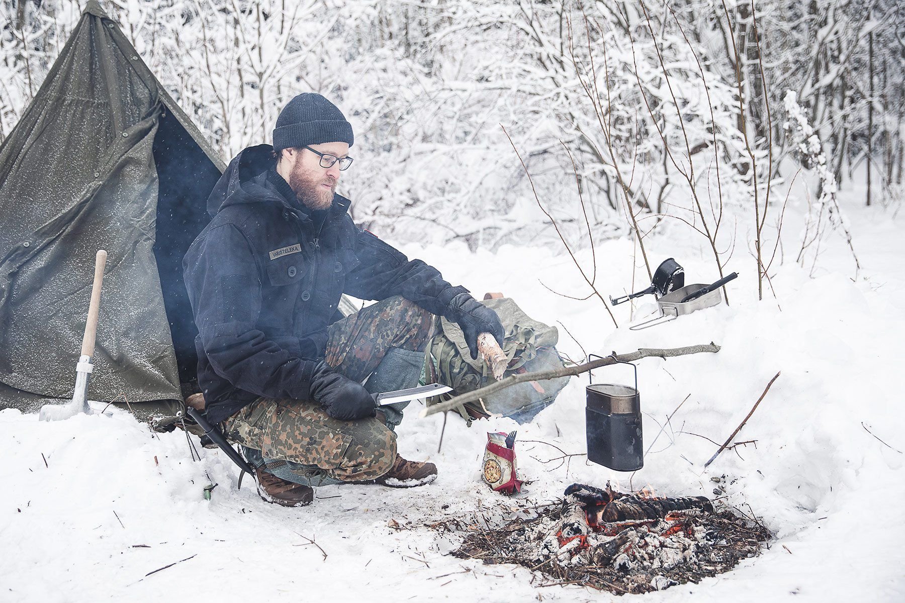 A person sitting before a camp fire cooking food.