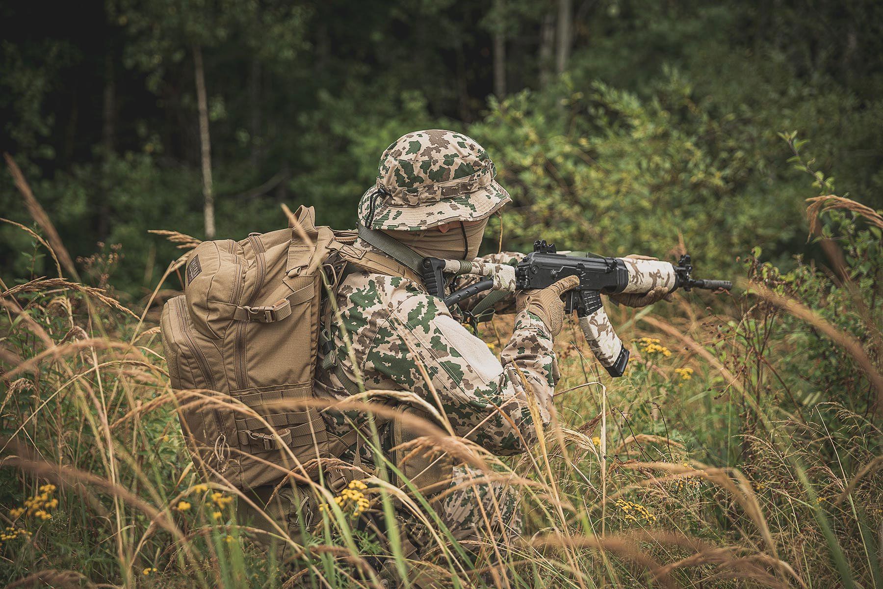 A person patrolling in tall grass wearing Särmä TST M04 camo fatigues.