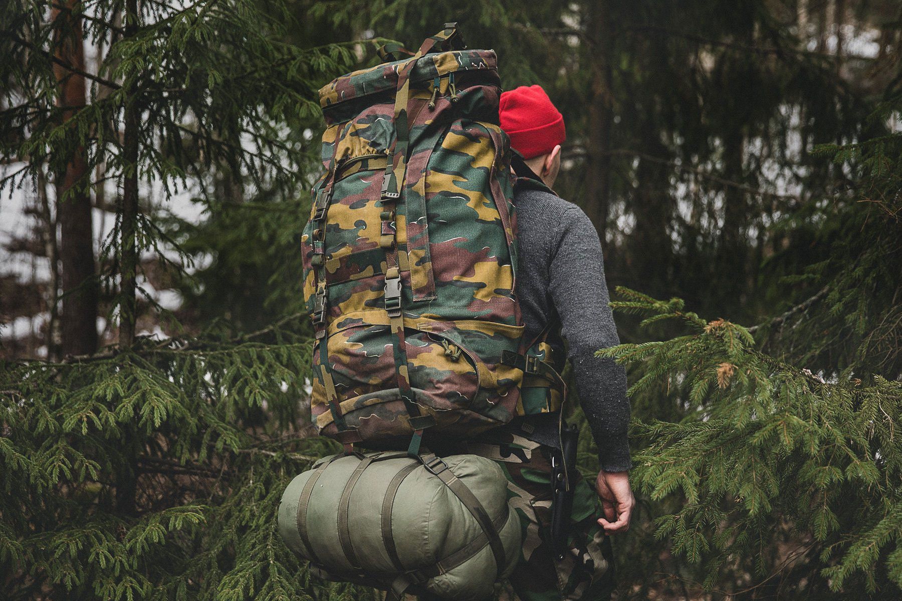 A person walking into the woods with a rucksack and a red Särmä merino wool cap.