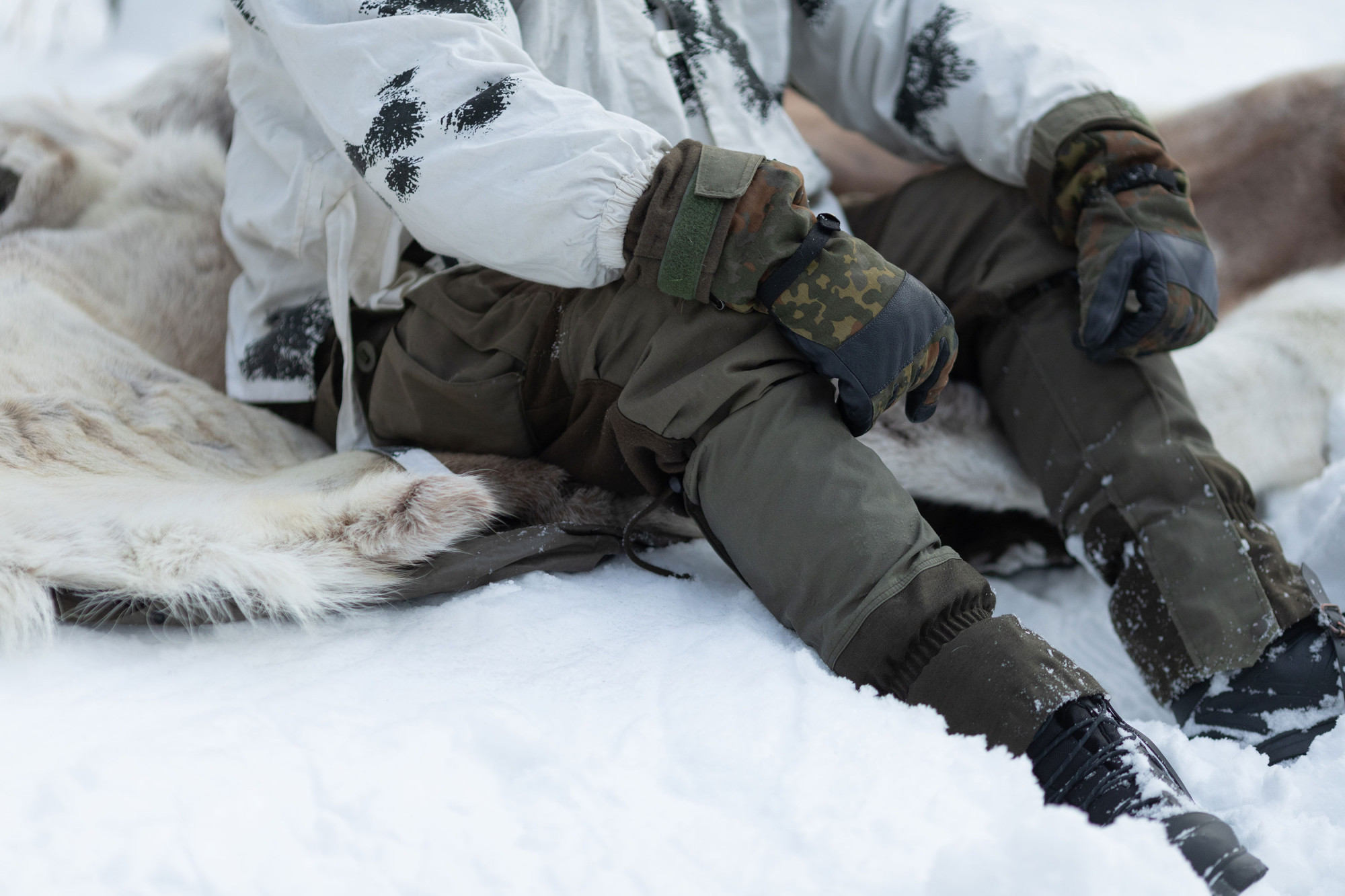 Winter hiker sitting on top of a reindeer hide in snow