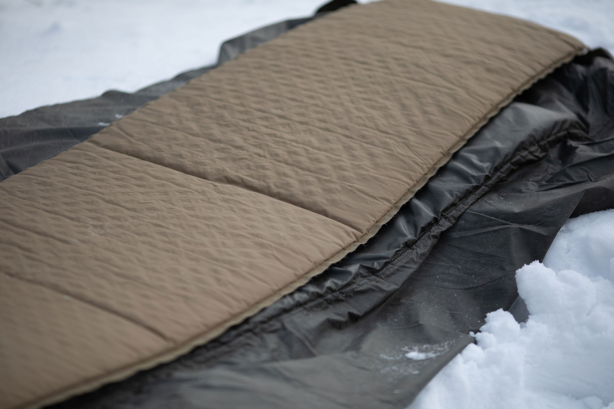 A thin inflatable sleeping pad on top of the Savotta FDF Sleeping Pad in snow
