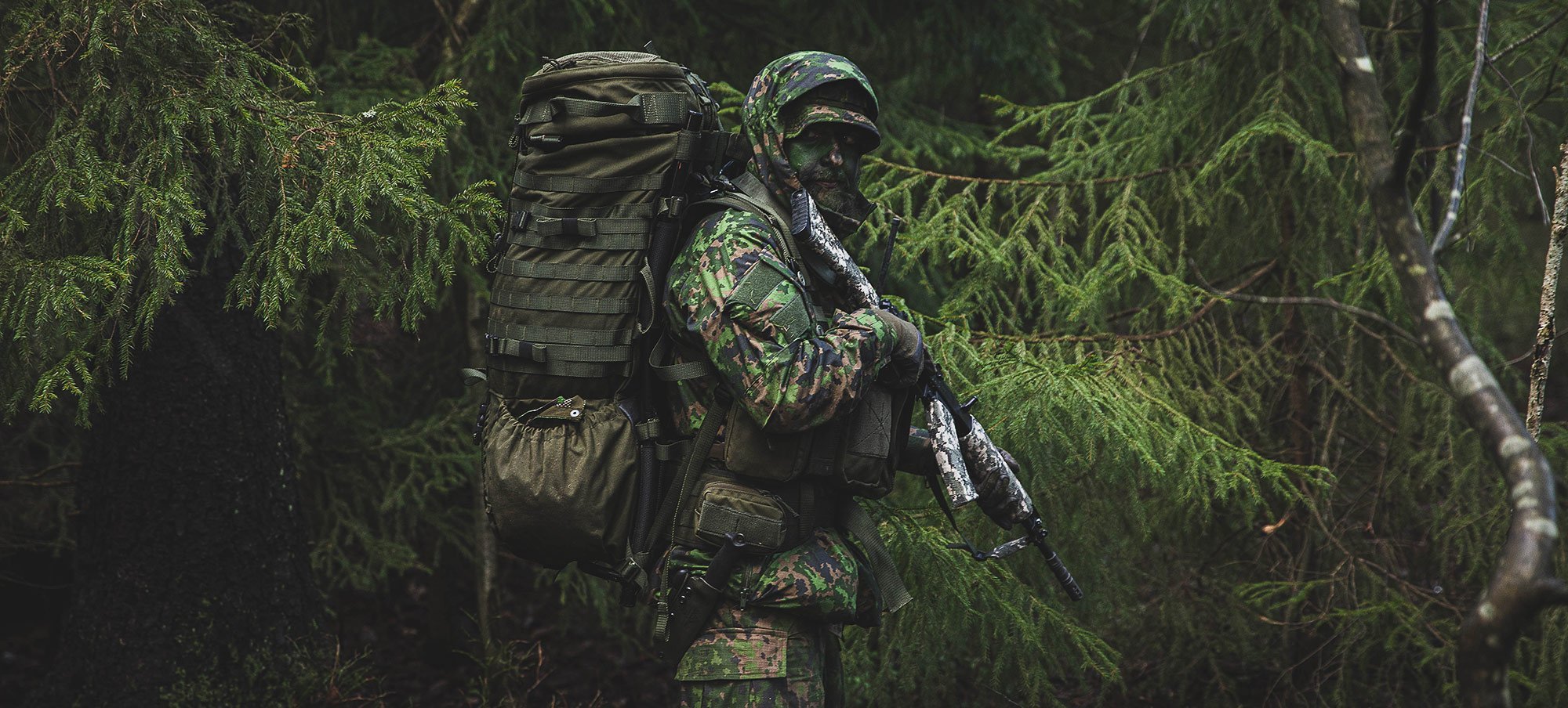 A camouflaged soldier in the woods carrying a rucksack