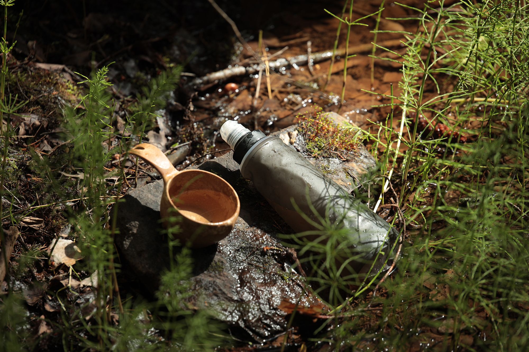 A water bottle with a water filter on top of a rock next to a kuksa