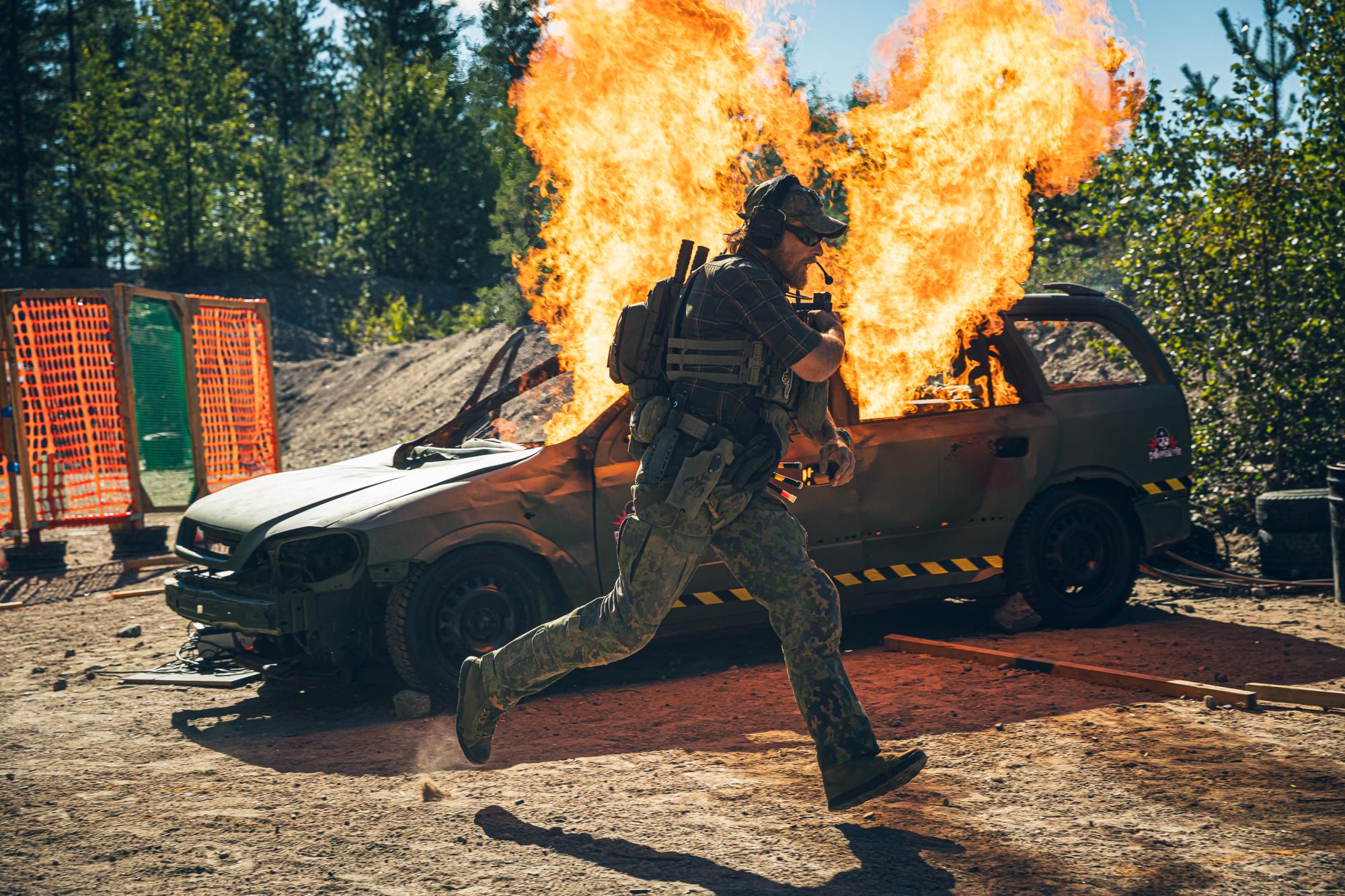 A man running in front of a burning car.