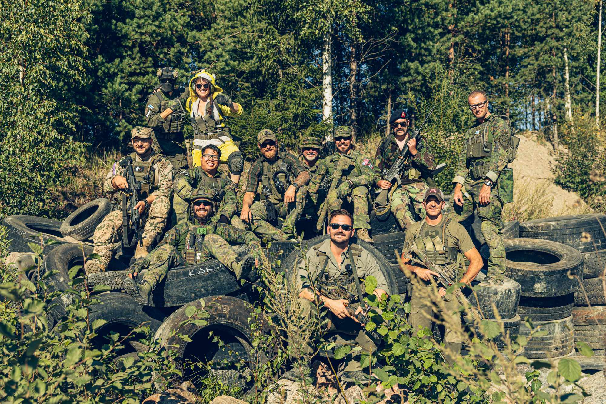 People in camo clothing gathered together to pose for the camera in front of a forest..