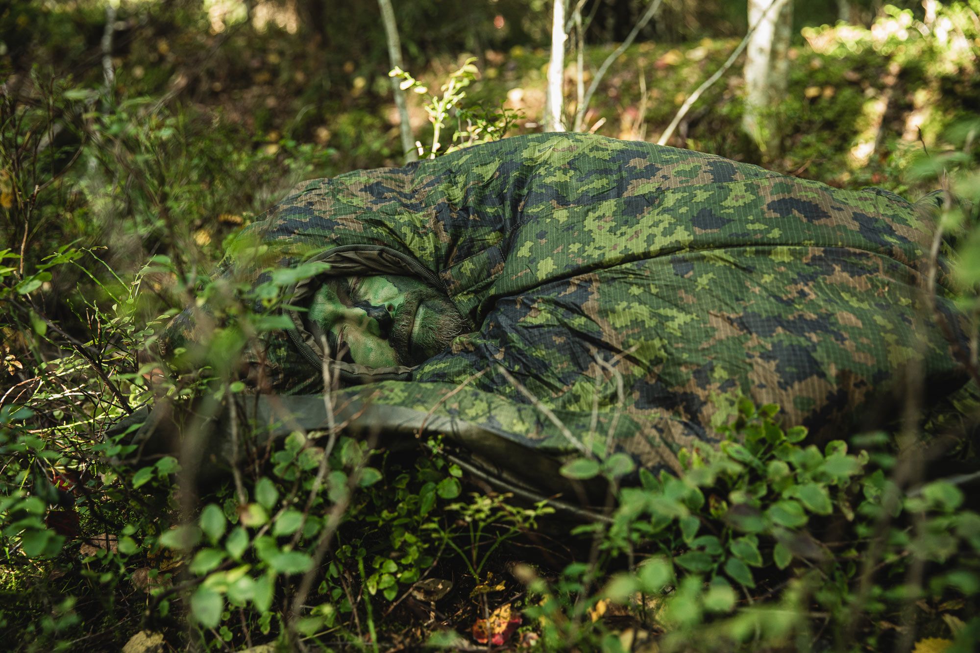 Man sleeping in a forest in an M05 camo sleeping bag.