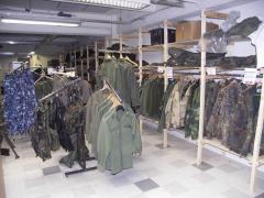 Wooden shelfs and some clothes racks with military surplus clothing hanging on them.