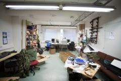 An office room with a couple of desks, a couch and stuff all over the place.