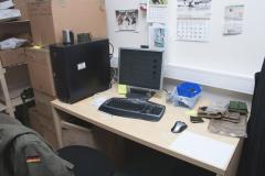 A small desk with a computer and some pictures hang on the wall.