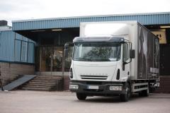 A humble sheet metal wall building with a medium sized truck in front of it.