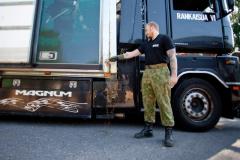 A man has broken a bottle of some brown liquid onto the side of a truck called Rankaisija VI.