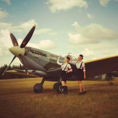 An old looking shot of a propeller plane and two sexy flight attendants.