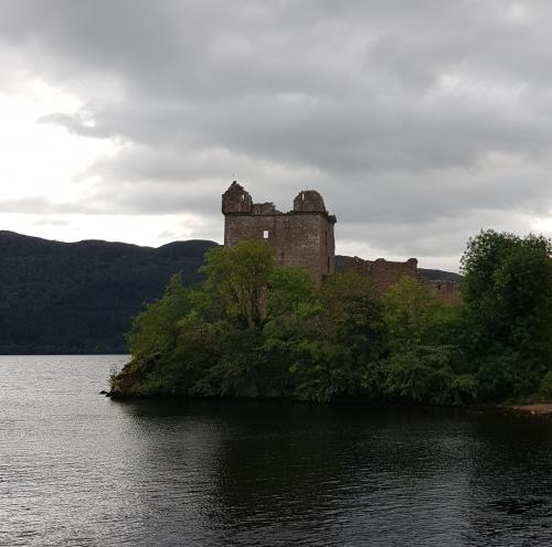 An old stone castle surrounded by water and hills.