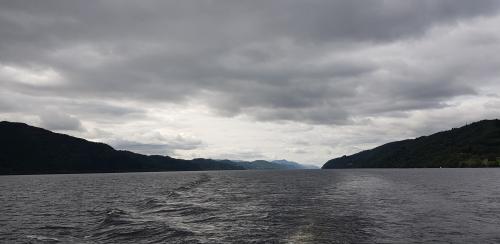 Stern waves of a boat  on a lake, hills and grey sky.