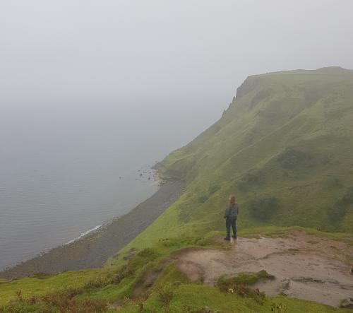 A long haired man gazeng at the sea on a grassy hill.