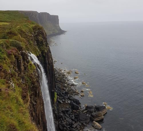 A steep cliff on the shore with a waterfall.